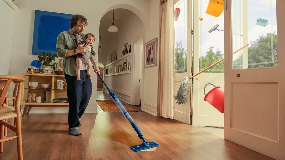 bebeğini taşıyan ve zemini temizlemek için Philips OneUp Elektrikli Paspas kullanan bir adam